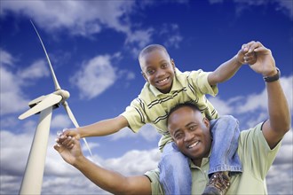 Happy african american father and son with wind turbine over blue sky