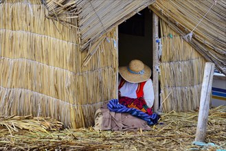 Indigenous woman embroidering in front of the reed hut on a Uro floating island