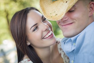 Happy mixed-race romantic couple with cowboy hat flirting in the park