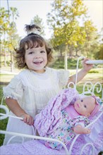 Adorable young baby girl playing with her baby doll and carriage outdoors