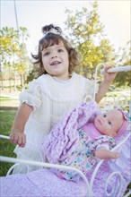 Adorable young baby girl playing with her baby doll and carriage outdoors