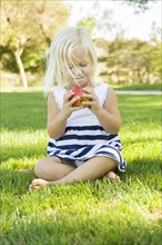 Cute little girl sitting and eating apple outside on the grass