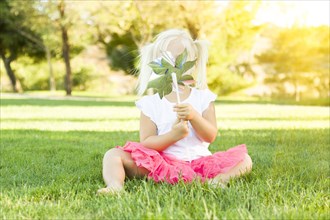 Cute little girl sitting in grass blowing on pinwheel toy