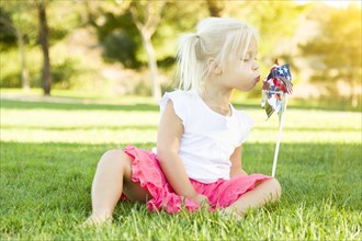 Cute little girl sitting in grass blowing on pinwheel toy