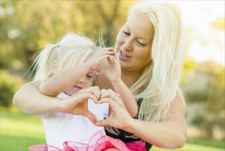 Cute little girl with mother making heart shape with hands outdoors