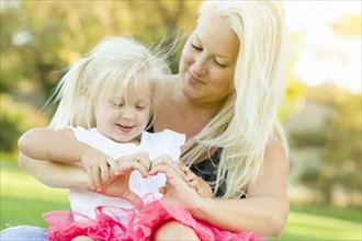 Cute little girl with mother making heart shape with hands outdoors