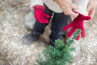 Caring mother putting red mittens on child near small christmas tree abstract with snow effect