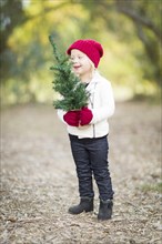 Baby girl in red mittens and cap holding small christmas tree outdoors