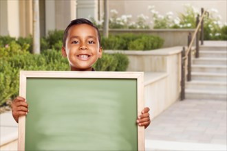 Happy hispanic boy holding blank chalk board on school campus