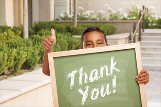 Happy hispanic boy giving thumbs up holding thank you chalk board outside on school campus
