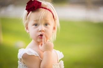 Beautiful adorable little girl with her finger on her mouth wearing white dress in A grass field