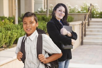 Happy hispanic boy with backpack on school campus and teacher behind