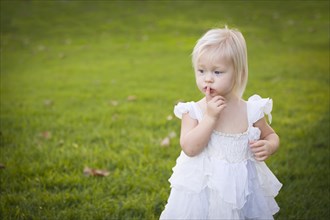 Beautiful adorable little girl with her finger on her mouth wearing white dress in A grass field