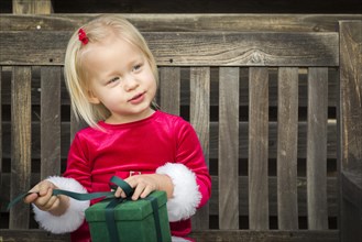Adorable little girl unwrapping her gift on a bench outside