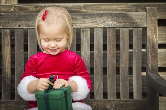 Adorable little girl unwrapping her gift on a bench outside