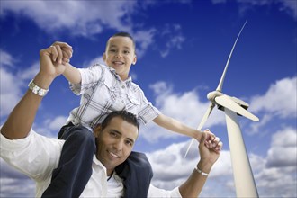 Happy hispanic father and son with wind turbine over blue sky