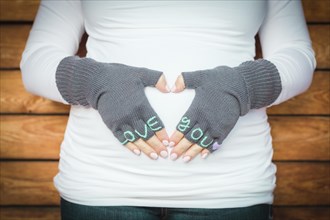 Pregnant woman holds her stomach with love you mittens on