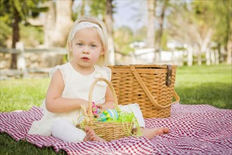 Cute baby girl enjoys enjoying her easter eggs on picnic blanket in the grass