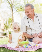Loving grandfather and granddaughter coloring easter eggs together on picnic blanket at the park