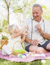 Loving grandfather and granddaughter coloring easter eggs together on picnic blanket at the park