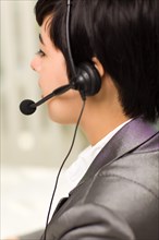 Profile of an attractive young mixed-race woman smiles wearing headset in an office setting