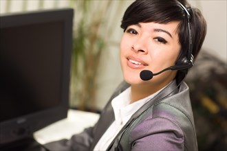 Attractive young mixed-race woman smiles wearing headset near her computer in an office setting
