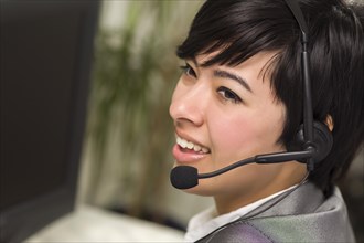 Attractive young mixed-race woman smiles wearing headset near computer monitor
