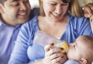 Happy attractive mixed-race couple bottle feeding their son