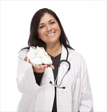 Attractive hispanic female doctor or nurse holding out baby shoes isolated on a white background