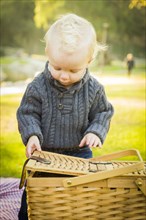 Adorable little blonde baby boy opening a picnic basket outdoors at the park