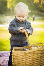 Adorable little blonde baby boy opening a picnic basket outdoors at the park