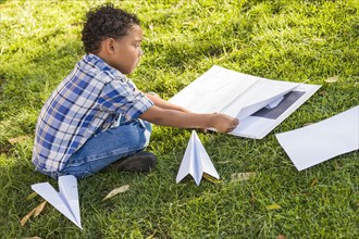 mixed-race boy learning how to fold paper airplanes outdoors on the grass