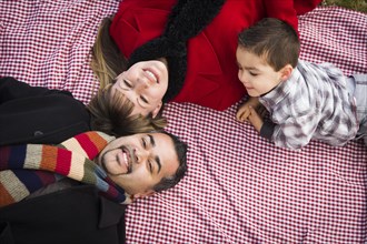 Young mixed-race family in winter clothing laying on their backs on picnic blanket in the park together