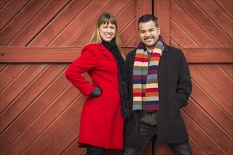 Young mixed-race couple portrait in winter clothing against barn door
