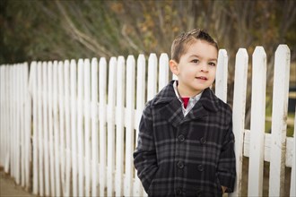 Young mixed-race boy waiting for school bus along fence outside