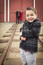 Young adorable mixed-race boy at train depot with parents smiling behind