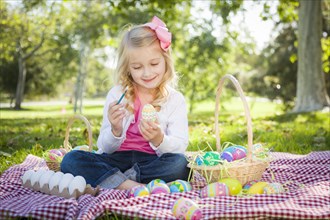 Cute young girl happily coloring her easter eggs with paint brush in the park