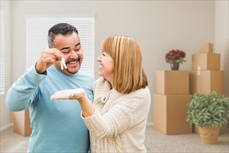 mixed-race couple holding house keys inside empty room with moving boxes