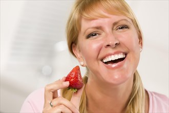 Pretty smiling blonde woman holding strawberry in her kitchen