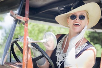 Attractive young woman in twenties outfit driving an antique automobile