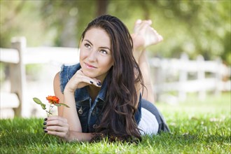 Attractive mixed-race girl daydreaming laying in grass outdoors with flower
