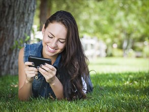 Attractive happy mixed-race young female texting on her cell phone outside laying in the grass