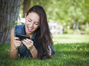Attractive happy mixed-race young female texting on her cell phone outside laying in the grass