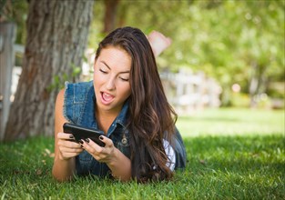 Shocked mixed-race young female texting on her cell phone outside laying in the grass