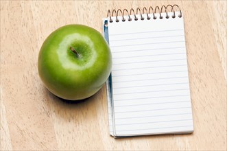 Pad of paper and apple on a wood background
