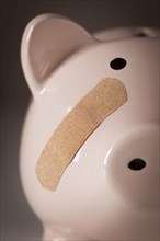 Piggy bank with bandage on face on dramatic gradated background