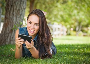 Shocked mixed-race young female texting on her cell phone outside laying in the grass