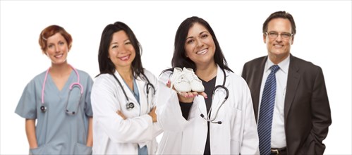 Attractive hispanic female doctor or nurse holding out baby shoes and support staff behind isolated on a white background