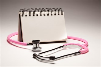 Blank spiral note pad and pink pediatric stethoscope on gradated background