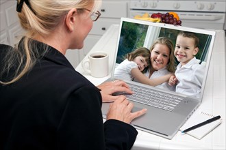 Woman in kitchen using laptop see friends and family. screen can be easily used for your own message or picture. picture on screen is my copyright as well